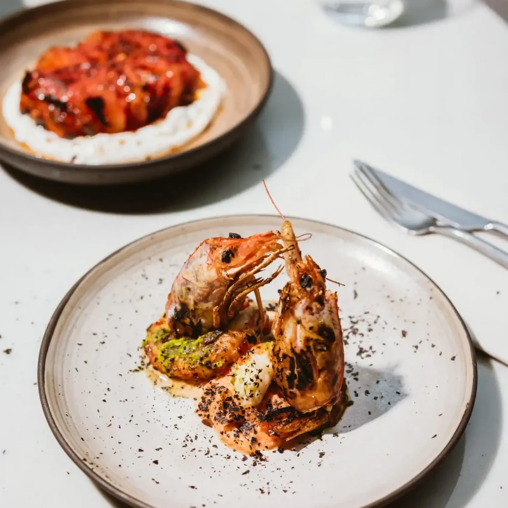 Two plates of food, one with shrimps and one with meat on a table outside in the zazatam summer venue. VIENNA, RESTAURANT, FINE DINING